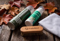 Imprägnierspray, Schaumreiniger, Schuhbürste und Waschbeutel auf Holz im herbstlichen Licht